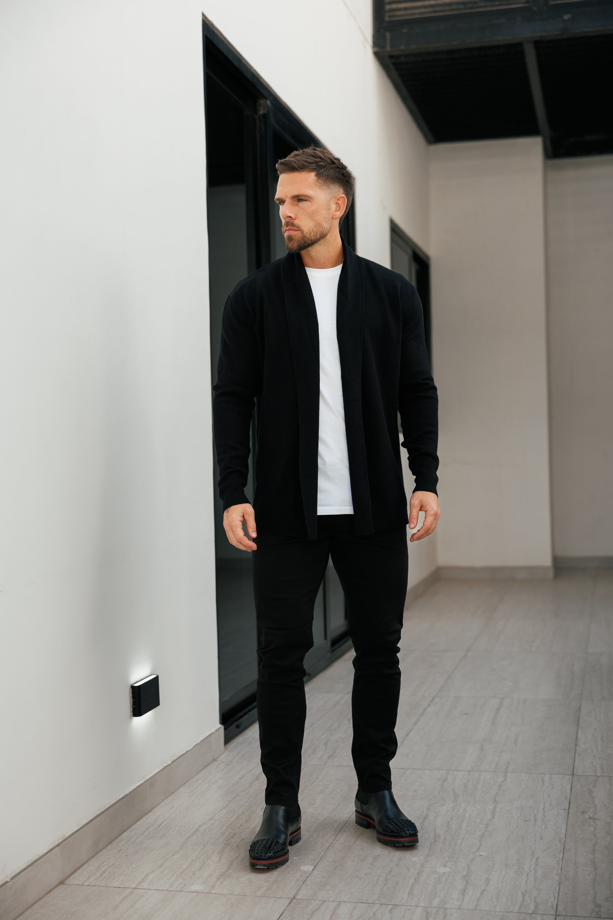 Man in a black jacket and pants standing in a modern indoor setting.