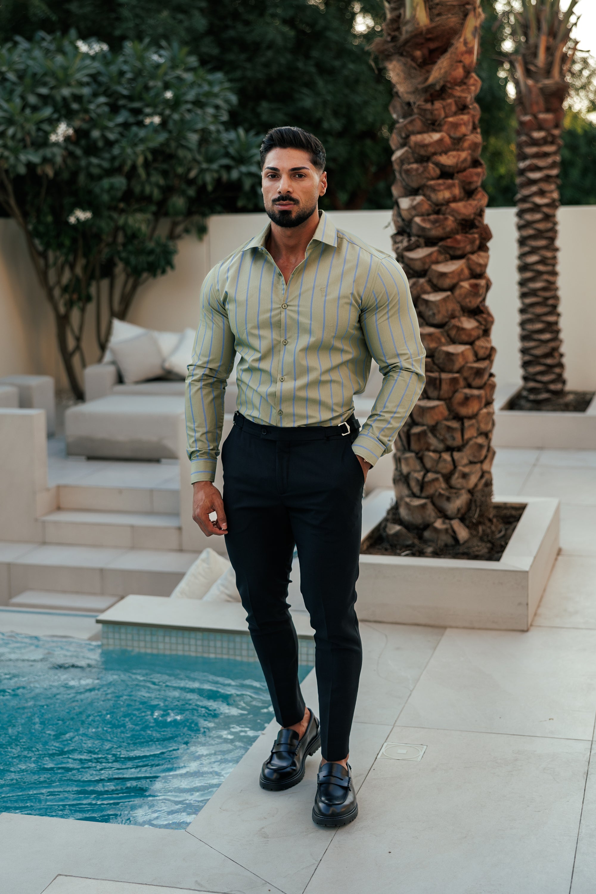 Man standing by a poolside with palm trees and outdoor furniture in the background