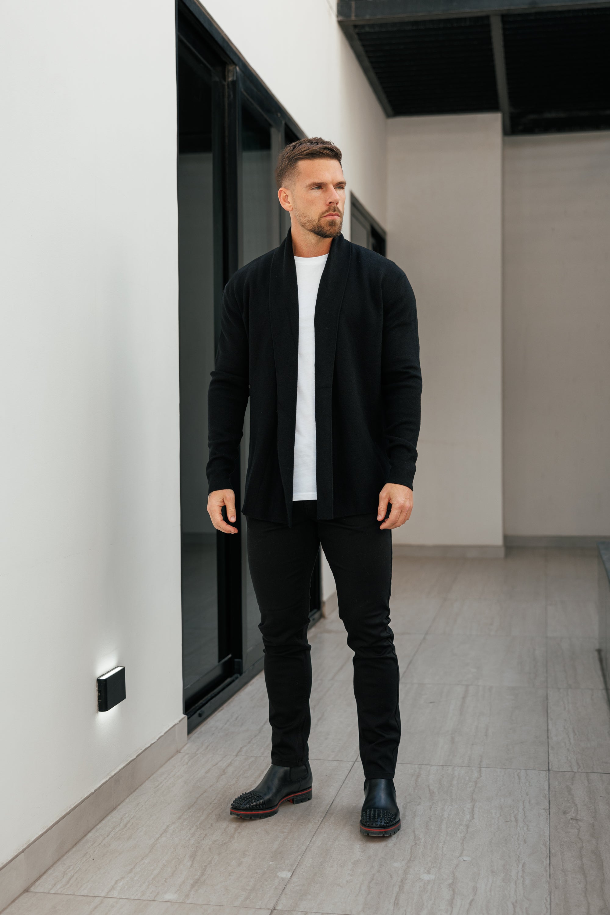 Man in a black jacket and pants standing in a modern indoor setting