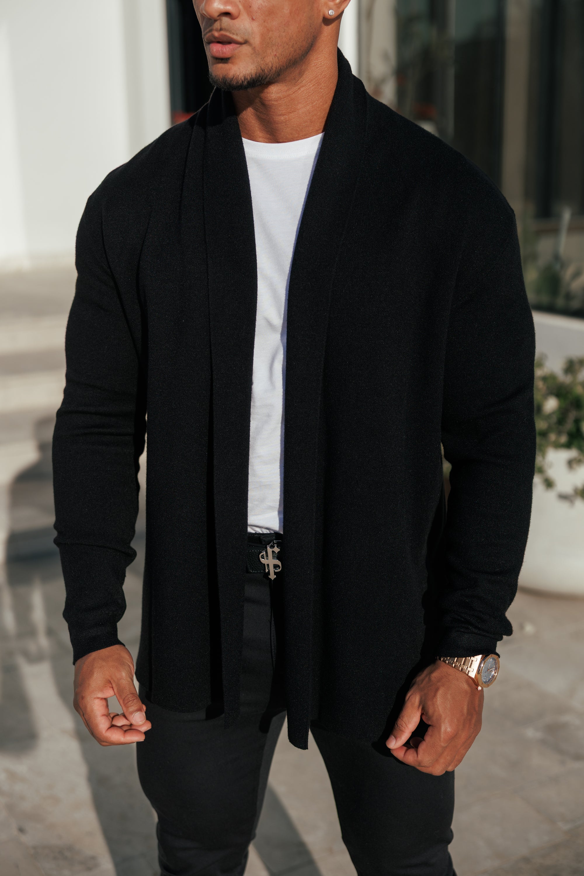 Man wearing a black cardigan over a white shirt with a blurred background